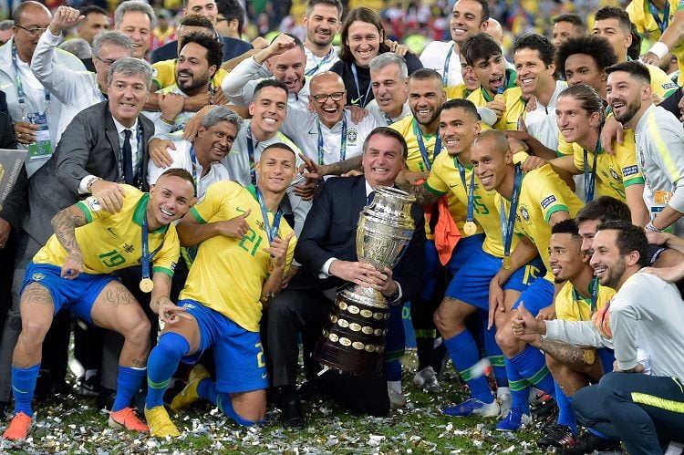TOPSHOT - Brazilian President Jair Bolsonaro holds the Copa America trophy as members of the Brazilian national team celebrates after winning the title by defeating Peru in the final match of the football tournament at Maracana Stadium in Rio de Janeiro, Brazil, on July 7, 2019. (Photo by Carl DE SOUZA / AFP)