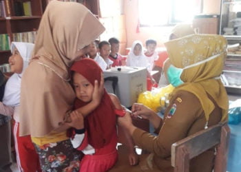 IMUNISASI MR. Petugas Puskesmas Rawat Jalan Kecamatan Palas, Lampung Selatan, memberikan imunisasi vaksin MR di Desa Pematangbaru, Rabu (14/8). Pelayanan imunisasi MR diberikan karena memasuki Bulan Imunisasi Anak Sekolah. (LAMPUNG POST/ARMANSYAH)