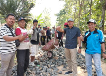 TERJUN LANGSUNG. Kepala Tiyuh Kibang Budijaya Tobroni (baju hitam bertopi) di tengah aktivitas pengerjaan jalan onderlaag bersama warga. Pembangunan untuk memajukan tiyuh menjadi komitmen kepala tiyuh sampai masa jabatannya berakhir. (LAMPUNG POST/AHMAD SOBIRIN)