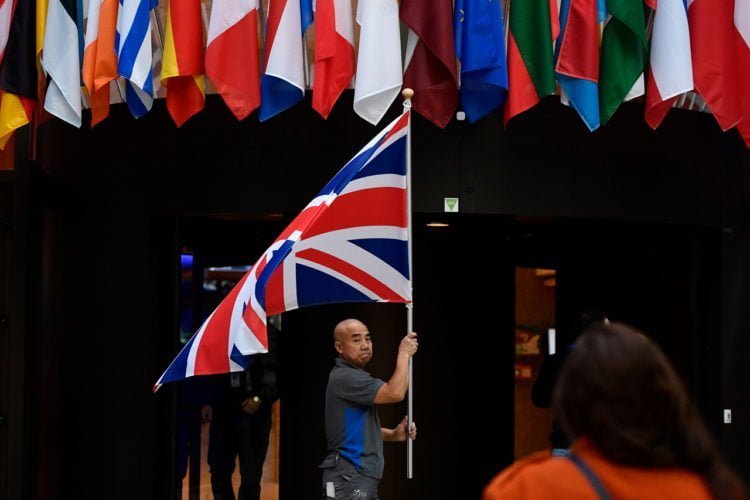 BREXIT. Seorang karyawan mengibarkan bendera Inggris di pintu masuk gedung Consilium di Markas Besar Uni Eropa Brussels, Senin (28/10).  Anggota Uni Eropa sepakat menunda Brexit hingga tiga bulan. (JOHN THYS/AFP)