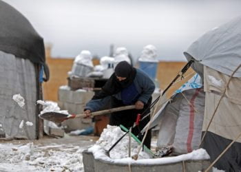 Seorang wanita membersihkan tumpukan salju di sebuah kamp di Tal Abyad, Suriah, 13 Februari 2020. (Foto: AFP/BAKR ALKASEM)