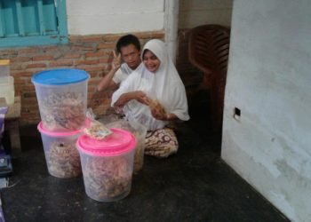 MENGEMAS PEYEK. Nur Khasanah, didampingi putra keduanya yang berkebutuhan khusus, Gilang, warga Dusun Tanjunganom, Desa Madukoro, Kecamatan Kotabumi Utara, mengemasi peyek yang akan dijual ke pelanggan, di rumahnya, Senin (10/2). LAMPUNG POST/YUDHI HARDIYANTO