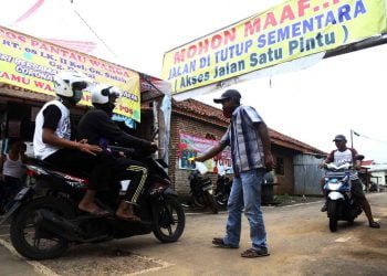 CEGAH COVID-19. Warga melintas di depan pintu masuk RT 8 Lk II Gang Damai, Gunungsulah, Bandar Lampung, saat dilakukan penyemprotan disinfektan, Minggu (5/4). Penyemprotan kawasan tersebut sebagai upaya mencegah dan memutus rantai penyebaran Covid-19 yang telah menyebar ke Kota Bandar Lampung.
LAMPUNG POST/ZAINUDDIN