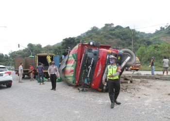 TRUK TERGULING. Polisi berada di lokasi truk bermuatan barang-barang ekspedisi yang terguling di turunan Jalan Ir Sutami, Sukabumi, Bandar Lampung, Rabu (15/7). Truk bernomor polisi BE-8837-AE tersebut diduga mengalami rem blong, sehingga tak dapat dikendalikan namun peristiwa itu menimbulkan korban jiwa.LAMPUNG POST/ZAINUDDIN