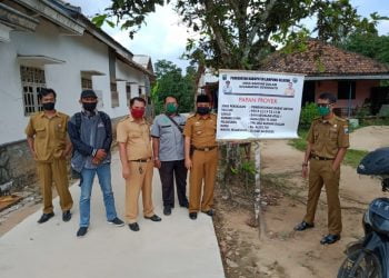 PAPAN PROYEK. Kepala desa dan sejumlah pamong desa lainnya berfoto bersama di depan papan proyek pembangunan infrastruktur jalan penghubung antardusun di Desa Bandardalam, Kecamatan Sidomulyo, Lampung Selatan, Minggu (5/7). LAMPUNG POST/PERDHANA WIBYSONO