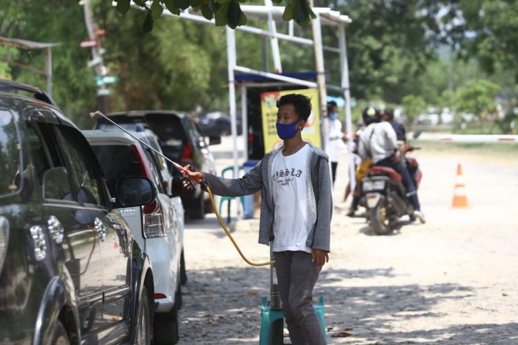 SEMPROTKAN CAIRAN DISINFEKTAN. Petugas menyemprotkan cairan disinfektan ke kendaraan pengunjung dan mengimbau pengunjung untuk mematuhi protokol kesehatan 3M di Pantai Mutun, Pesawaran, Kamis (29/10). Sejumlah tempat wisata pantai di Lampung mulai dipenuhi pengunjung dari luar kota saat libur panjang.LAMPUNG POST/ZAINUDDIN
