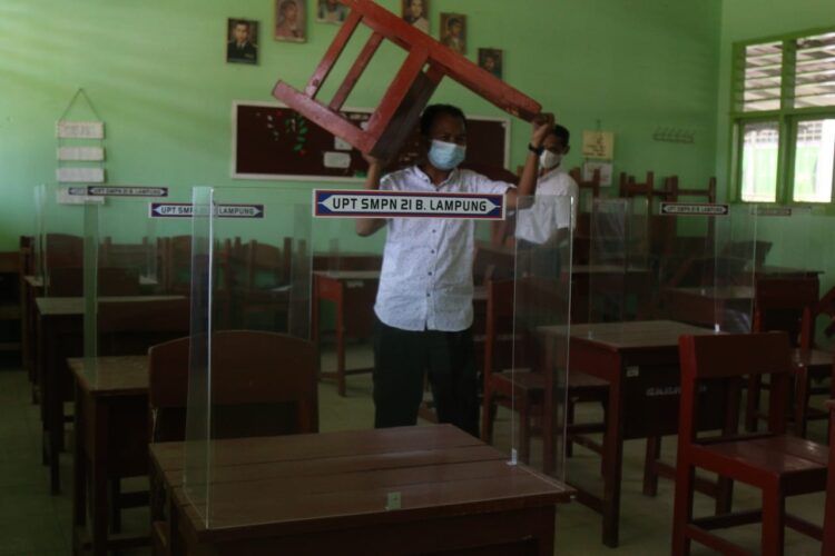 Guru SMPN 21 Bandar Lampung mempersiapkan ruangan yang telah disekat per mejanya untuk persiapan pembelajaran tatap muka (PTM) di sekolah tersebut, Jumat (26/8). (LAMPUNG POST/UMAR ROBANI)