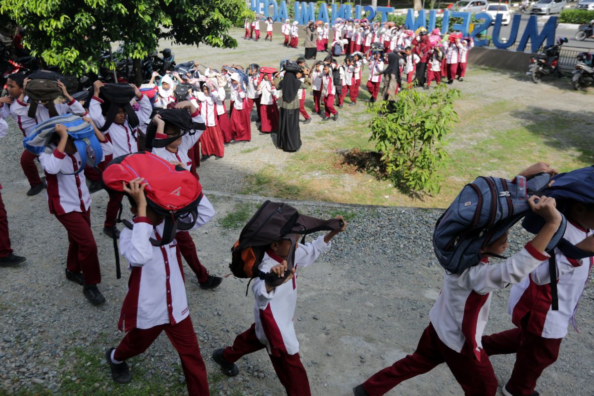 Pelajar melindungi kepala dengan tas saat mengikuti kompetisi simulasi evakuasi mandiri bencana gempa dan tsunami di Museum Tsunami. ANTARA FOTO/Irwansyah Putra